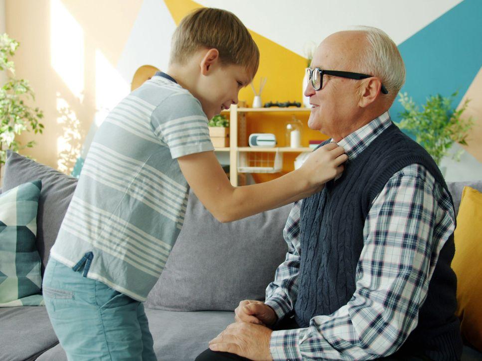 Grandson helping his elderly grandfather adjust his shirt collar, assisting a senior with loss of autonomy to get dressed