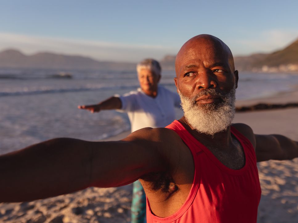 Homme âgé pratiquant une posture de yoga sur une plage