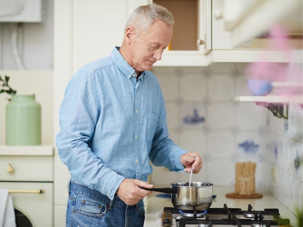 Senior man living alone safely cooking on a gas stove at home.